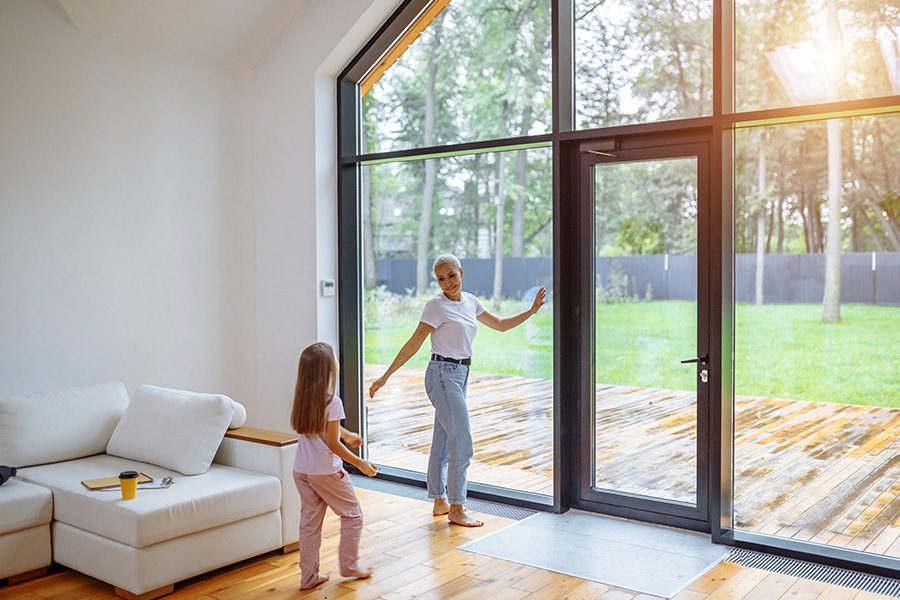 Personal Insurance - Mother and Daughter Standing Near a Panoramic Window Together Spending Time at Their New Modern Family Home
