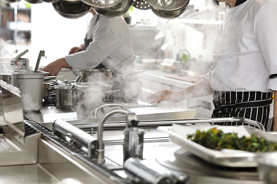 Specialized Business Insurance - Closeup of Chefs in a Hotel Restaurant Kitchen Cooking with Cooking Equipment Blurred in the Foreground